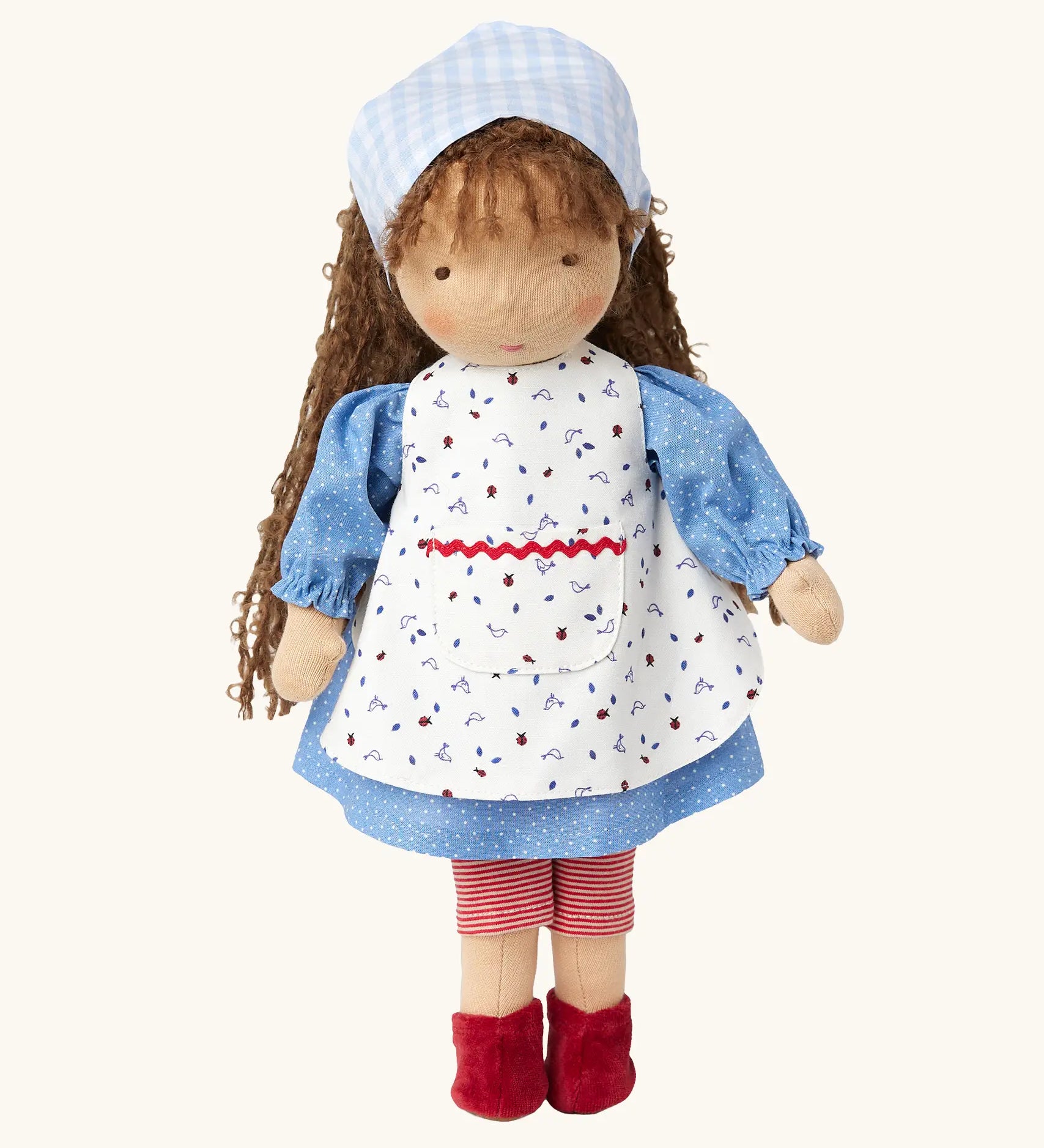 Käthe Kruse Waldorf doll Tilda with long brown hair and fair skin. Blue dotty dress wit red and white striped leggings underneath. White patterned apron and light blue gingham head scarf and red booties.