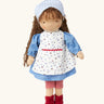 Käthe Kruse Waldorf doll Tilda with long brown hair and fair skin. Blue dotty dress wit red and white striped leggings underneath. White patterned apron and light blue gingham head scarf and red booties.