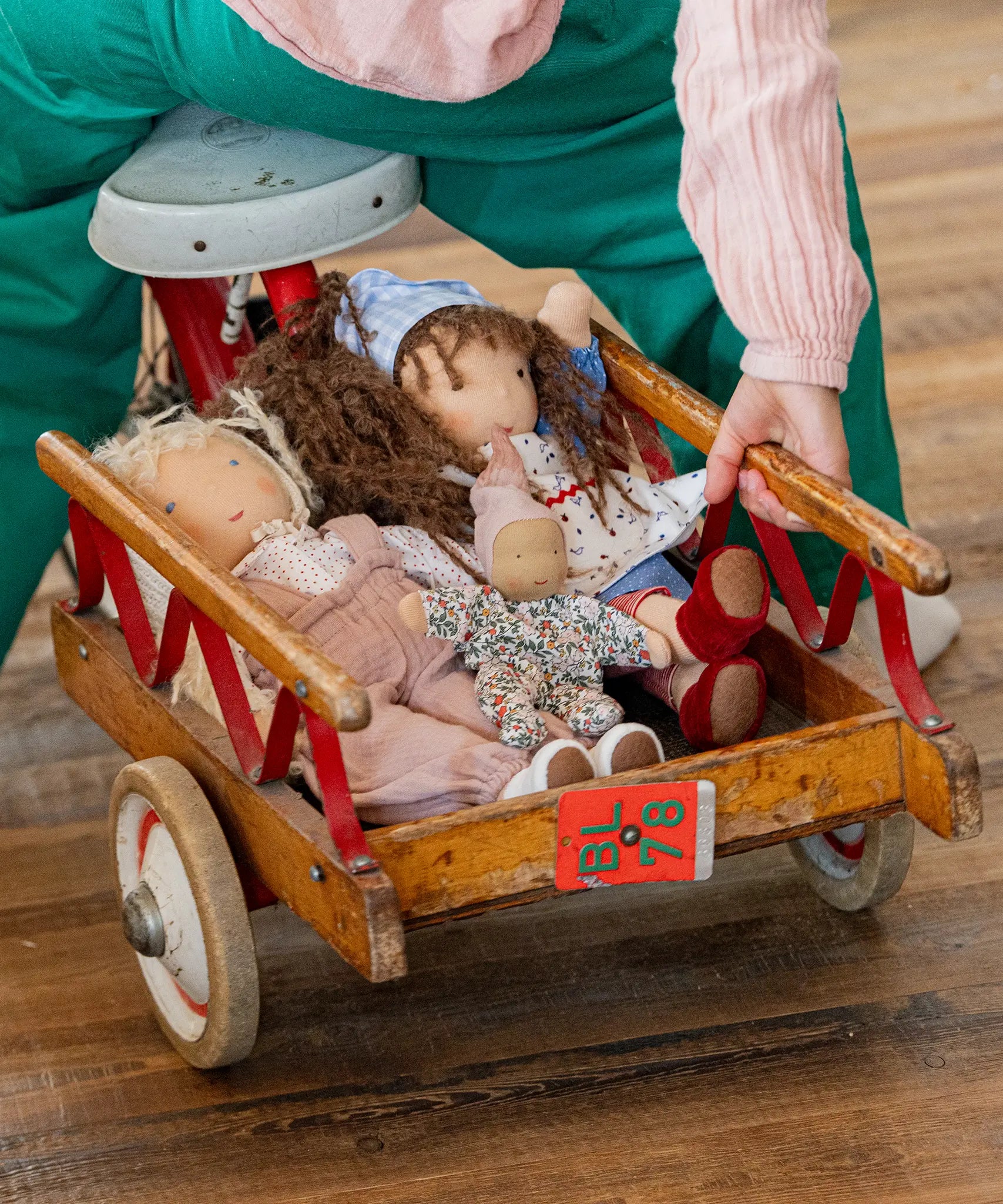 Käthe Kruse Waldorf doll Hannah and other dolls placed in the trailer of a bike ridden by a child. 