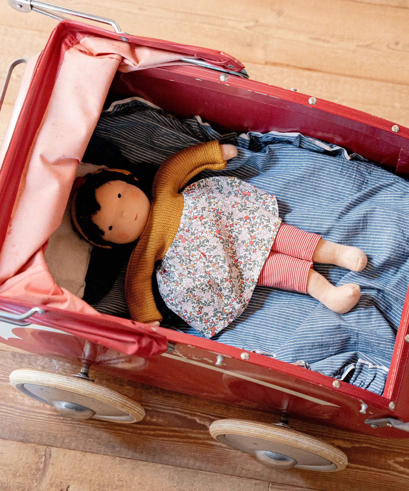 Käthe Kruse Waldorf Doll Kiki laying in a red doll's pram.
