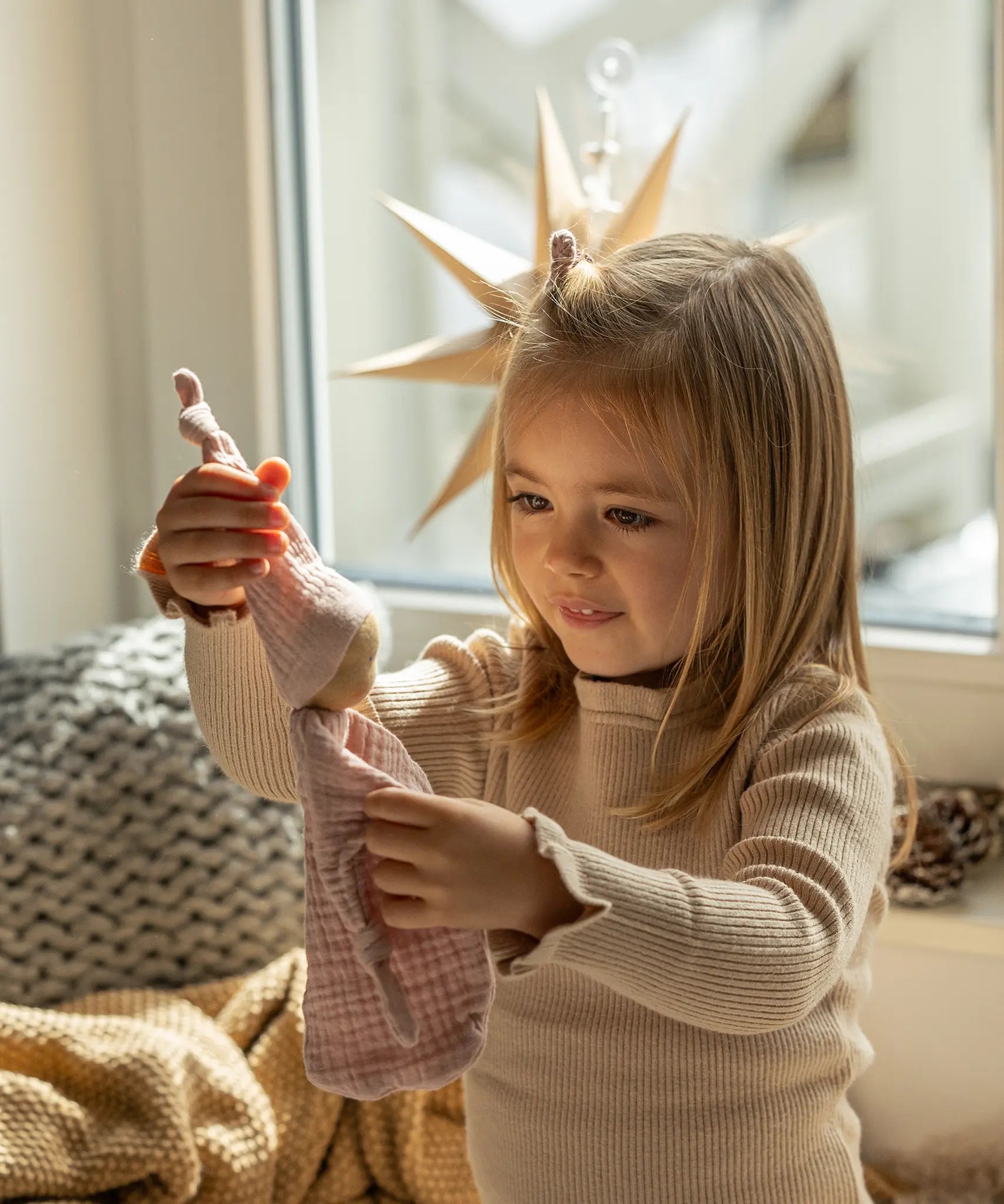 Käthe Kruse rose pink small Waldorf Imp doll comforter toy made with cotton muslin held in a child's hand. 