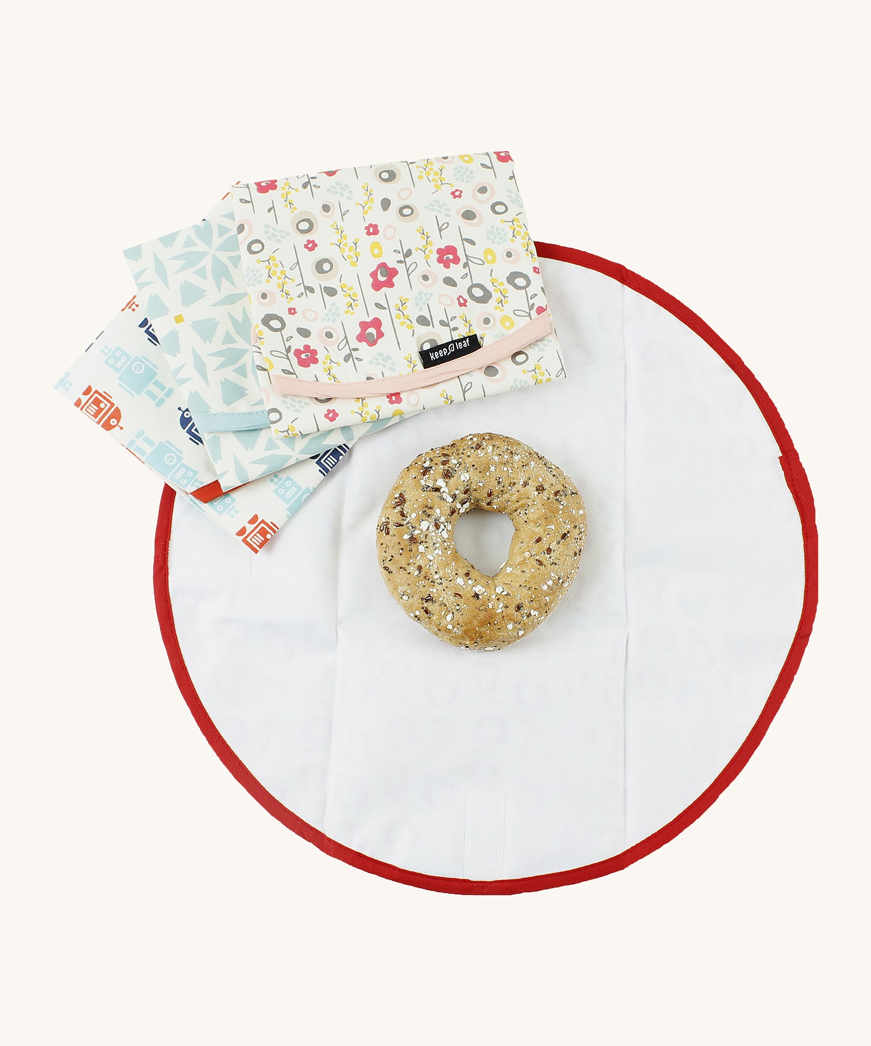 An open Keep Leaf food wrap with a bagel inside for size reference with a bloom, geo and robot food wrap on top 
