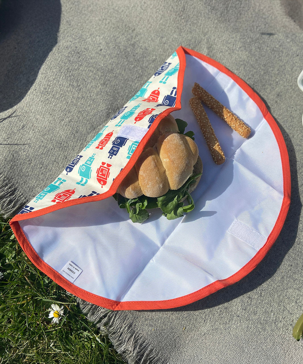 A close up view of the Keep Leaf food wrap in robot design on a grey blanket with a sandwich  packed inside