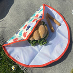 A close up view of the Keep Leaf food wrap in robot design on a grey blanket with a sandwich  packed inside