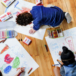 Top down view of children drawing with the Kitpas coloured non-toxic crayons on some large sheets of paper