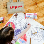 Top down view of a child drawing with the Kitpas non-toxic coloured crayons on a large sheet of white paper on the floor