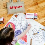 Top down view of a child drawing with the Kitpas non-toxic coloured crayons on a large sheet of white paper on the floor