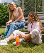 2 young adults holding the marigold and bay 16oz stainless steel reusable Klean Kanteen bottles by the loop handle. 