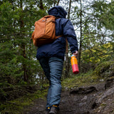 A man walking in woodland and holding the marigold kaleidoscope Klean Kanteen 16oz reusable rise insulated bottle by the white flip sports cap