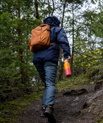 A man walking in woodland and holding the marigold kaleidoscope Klean Kanteen 16oz reusable rise insulated bottle by the white flip sports cap