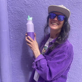 A woman holding the the orchid kaleidoscope 16oz Klean Kanteen stainless steel reusable rise bottle against a purple wall 
