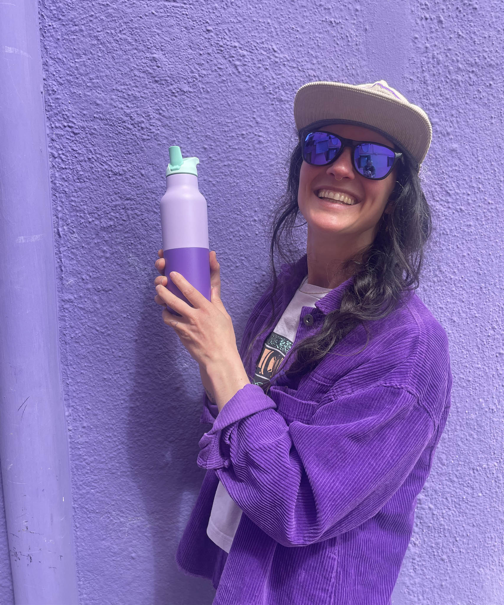 A woman holding the the orchid kaleidoscope 16oz Klean Kanteen stainless steel reusable rise bottle against a purple wall 