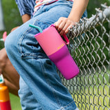 Child holding a 26oz stainless steel Klean Kanteen pink lemonade kaleidoscope tumbler with a aqua straw and sitting on a fence