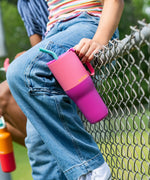 Child holding a 26oz stainless steel Klean Kanteen pink lemonade kaleidoscope tumbler with a aqua straw and sitting on a fence