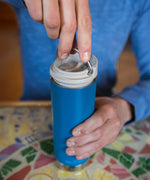 A close up of a person with a Klean Kanteen 16oz TKWide in corsair blue colour in their hand with taupe Cafe cap. 