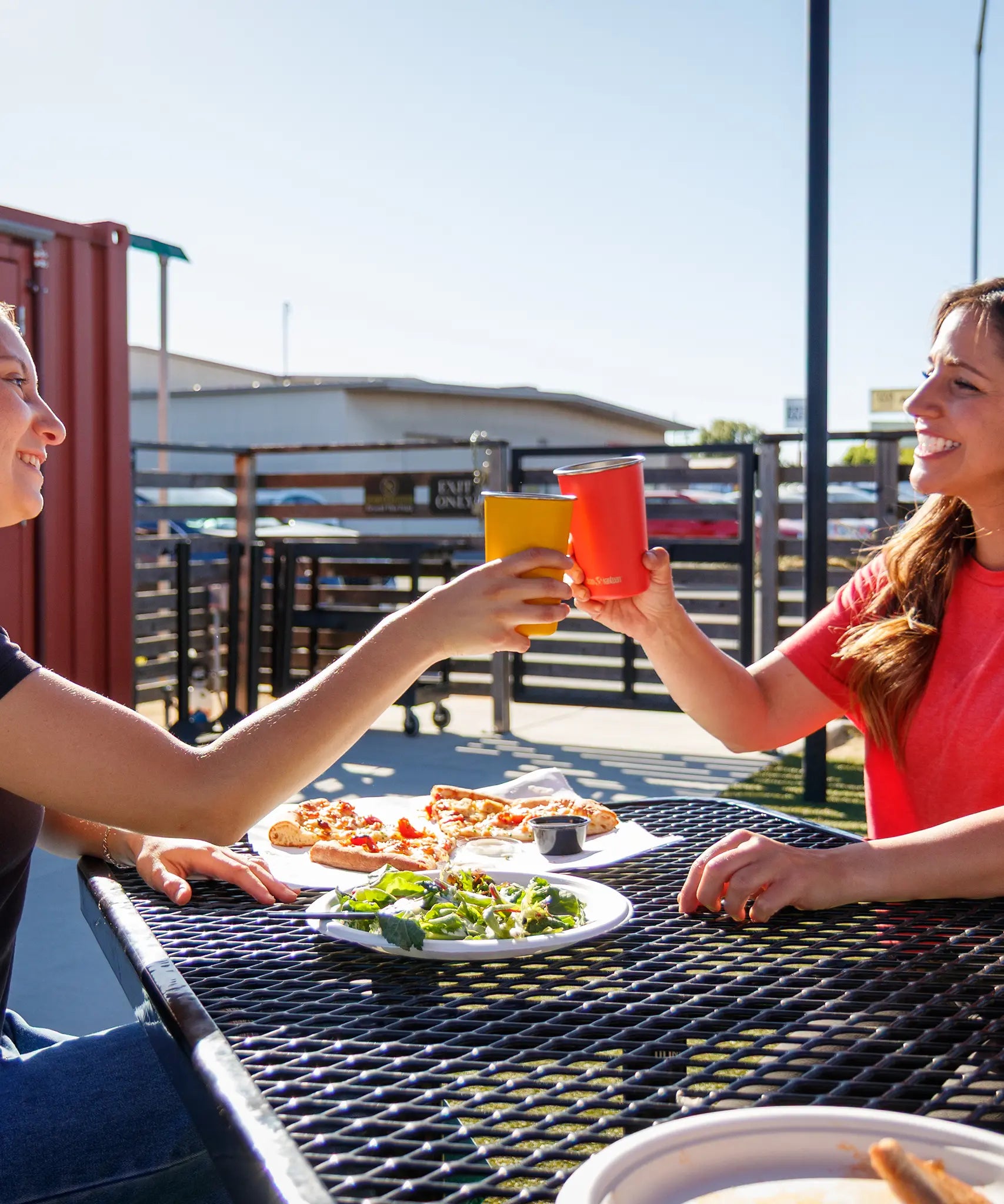 Two people with Klean Kanteen stainless steel 16oz pint cups in their hands making a cheering motion over a lunch table.