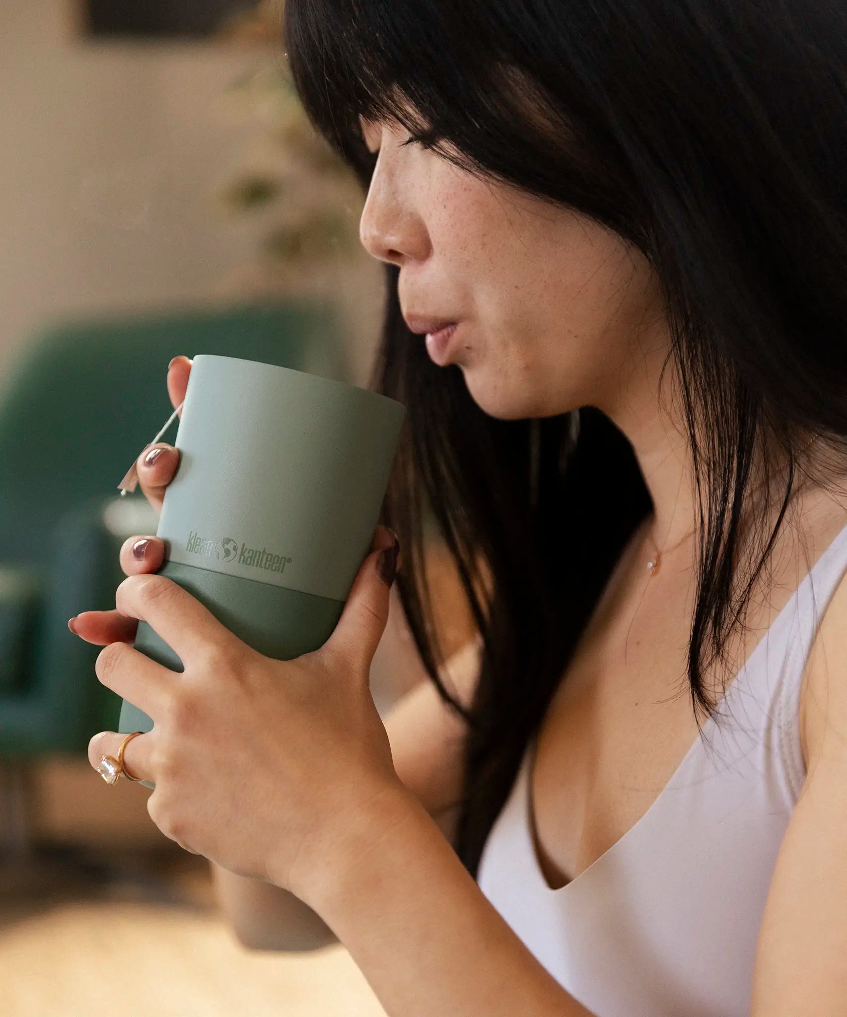 Adult hand blowing into a filled Klean Kanteen 16oz rise tumbler in iceberg green