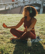 A woman doing yoga outside on grass next to a klean Kanteen 16oz reflect stainless steel  insulated bottle 