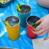 Three Klean Kanteen stainless steel 16oz pint cups in evening sky colours filled with drinks and placed on a blue blanket.