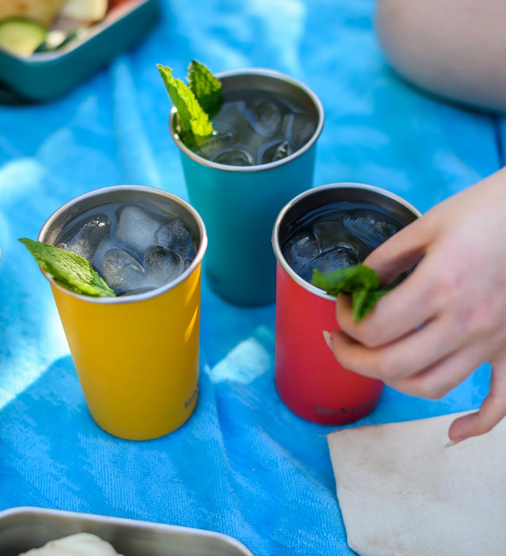 Three Klean Kanteen stainless steel 16oz pint cups in evening sky colours filled with drinks and placed on a blue blanket.