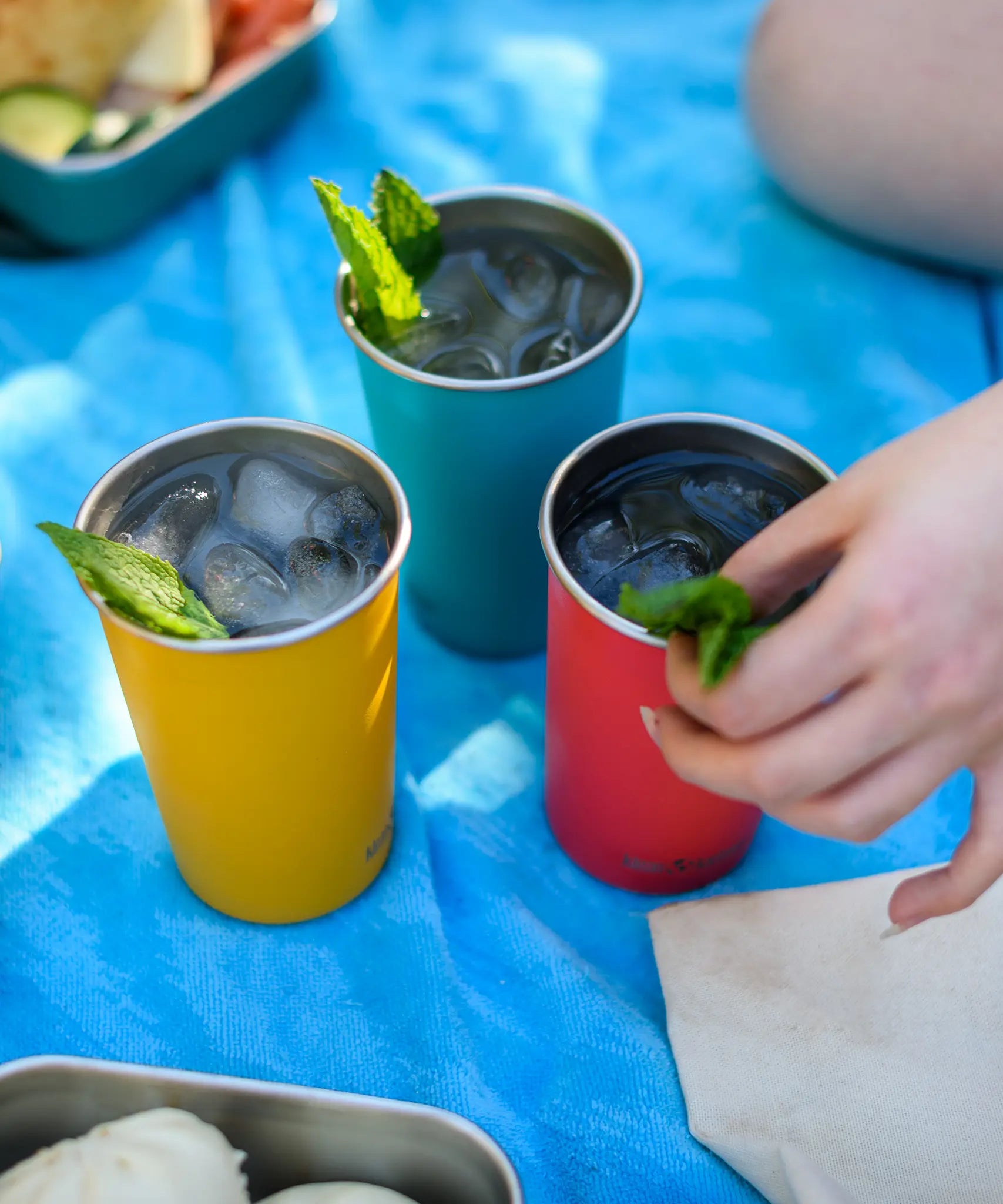 Three Klean Kanteen stainless steel 16oz pint cups in evening sky colours filled with drinks and placed on a blue blanket.