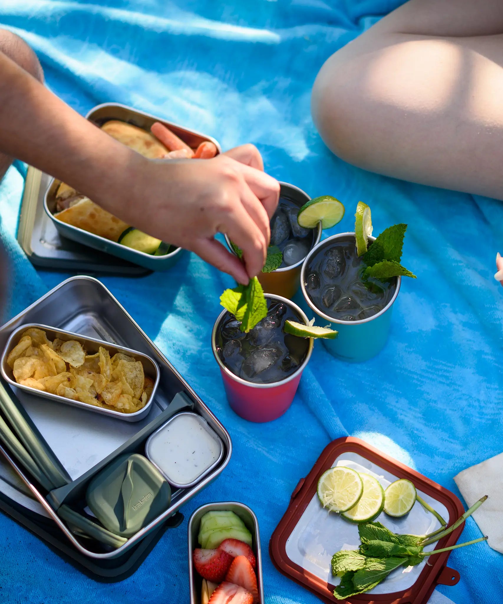 Three Klean Kanteen stainless steel 16oz pint cups in evening sky colours filled with drinks and placed on a blue blanket.