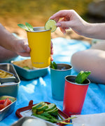 Yellow Klean Kanteen stainless steel 16oz steel pint cup filled with a drink in a person's hands with another person placing a lime on the side of the cup.