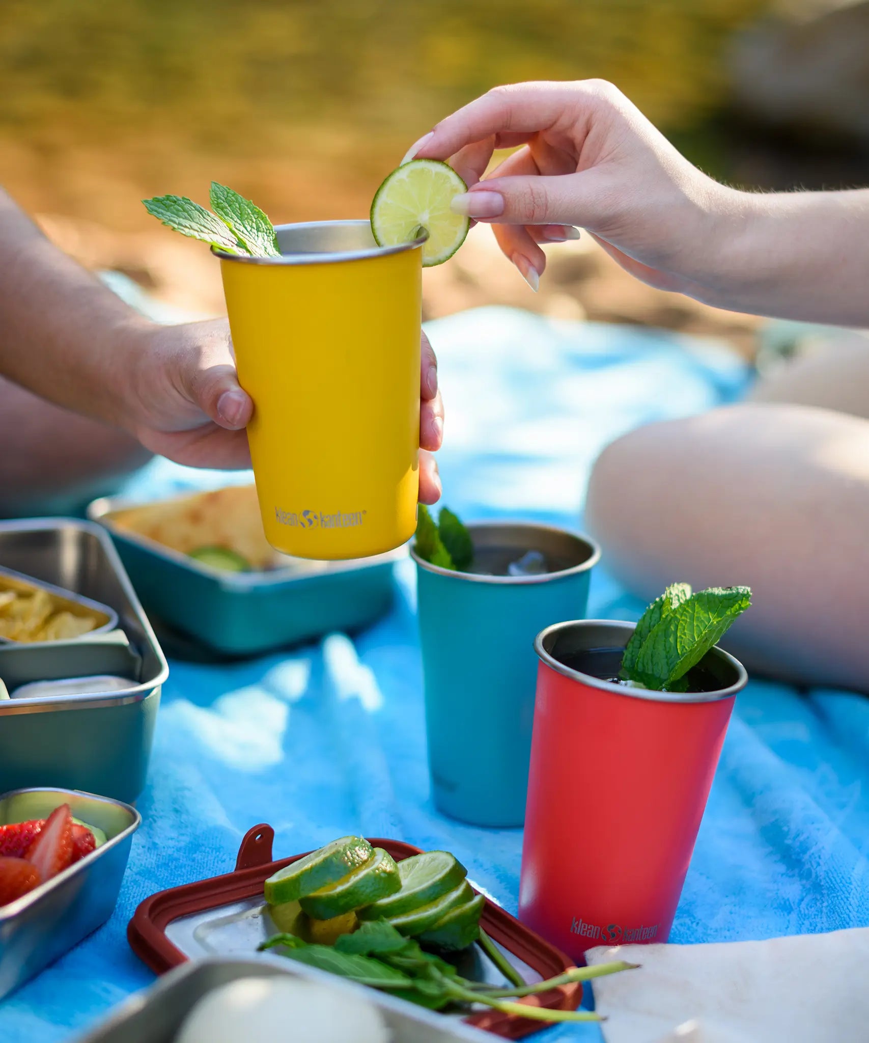 Yellow Klean Kanteen stainless steel 16oz steel pint cup filled with a drink in a person's hands with another person placing a lime on the side of the cup.