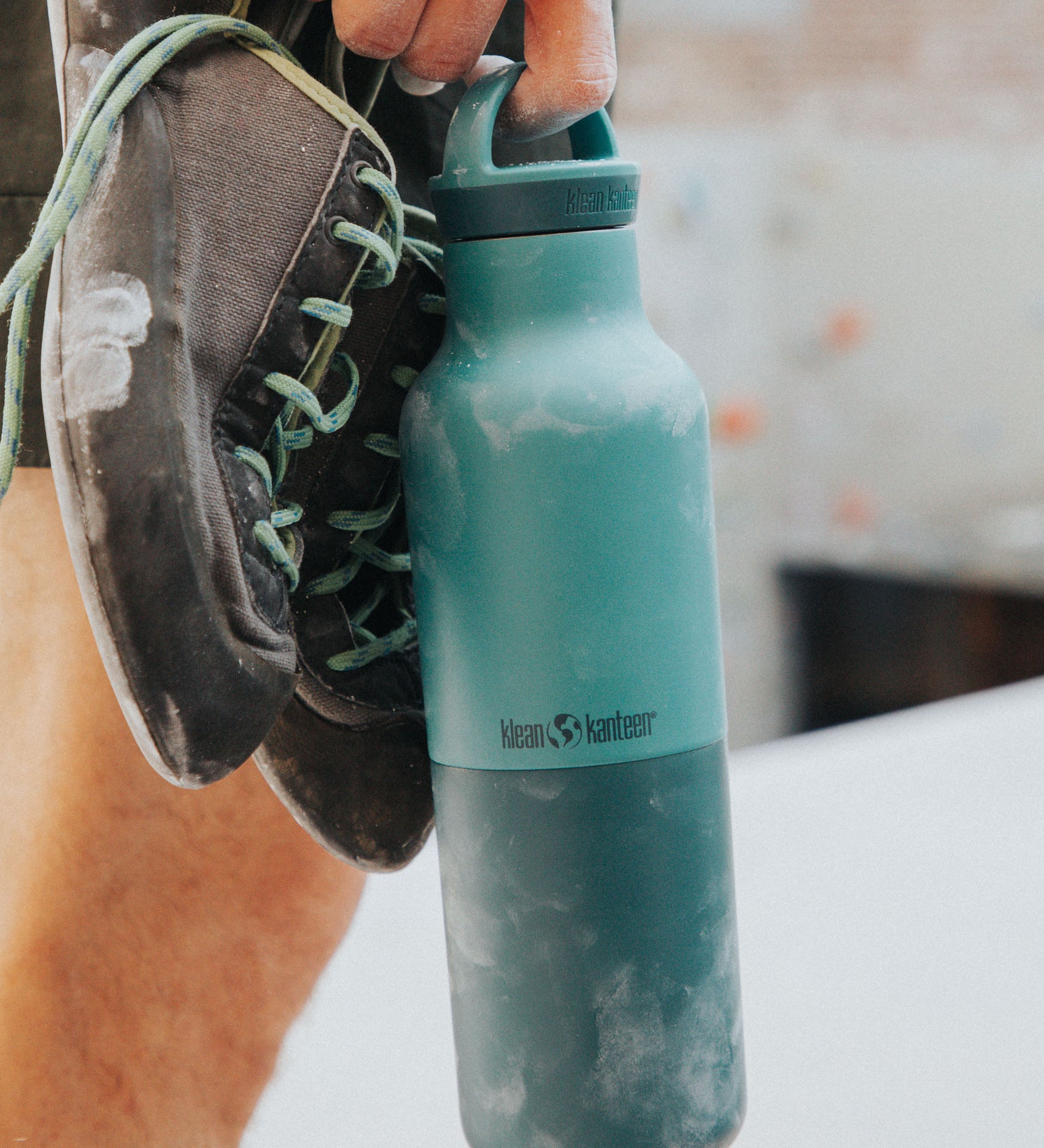 A climber holding the Klean Kanteen 20oz rise insulated Reusable Stainless Steel Water Bottle with loop cap in a Brittany blue colour. 