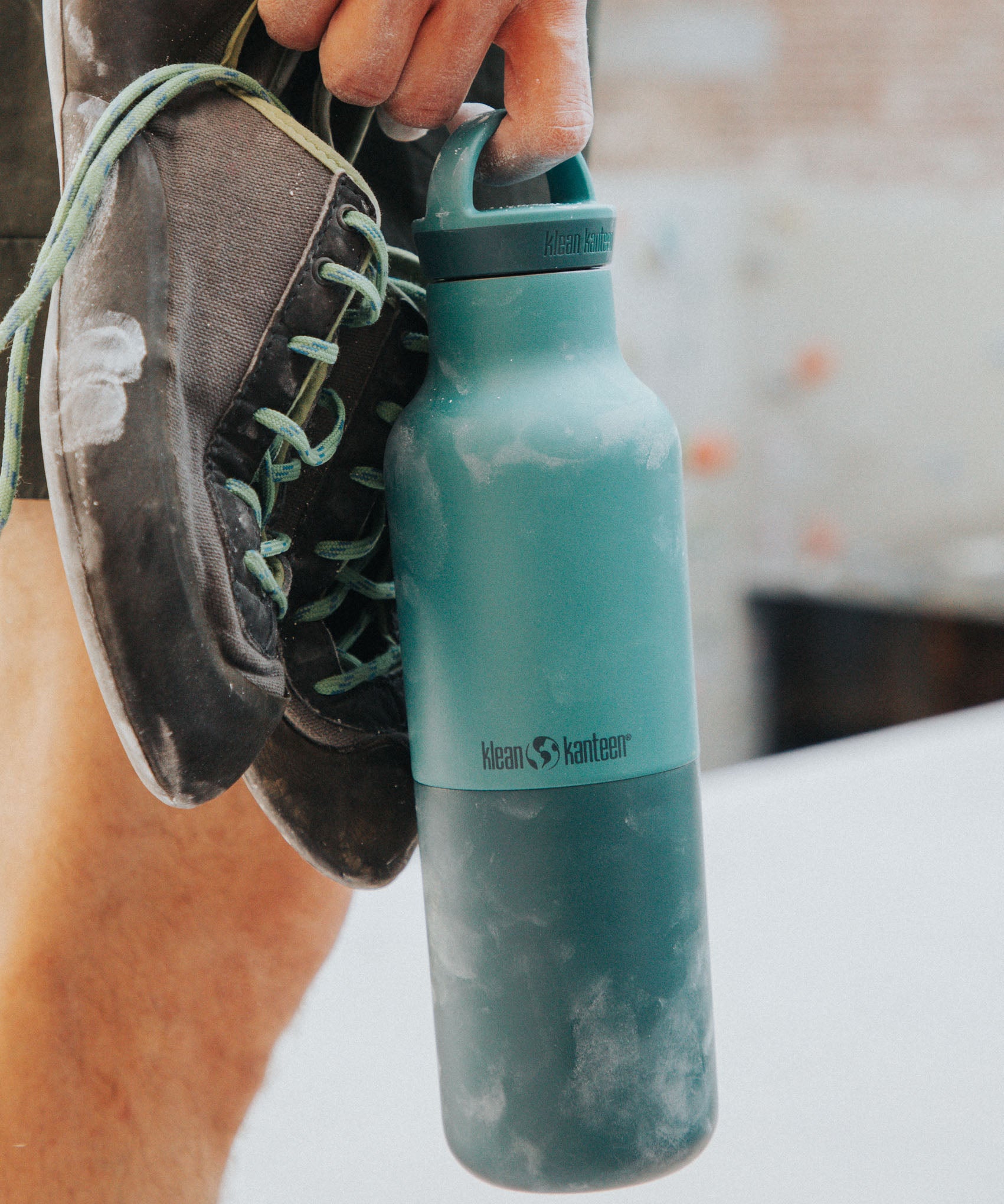 A climber holding the Klean Kanteen 20oz rise insulated Reusable Stainless Steel Water Bottle with loop cap in a Brittany blue colour. 