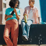 2 women sitting on a barrier and holding the 20oz klean Kanteen rise insulated classic bottles in black and acacia. A Reusable Stainless Steel Water Bottle with loop cap 