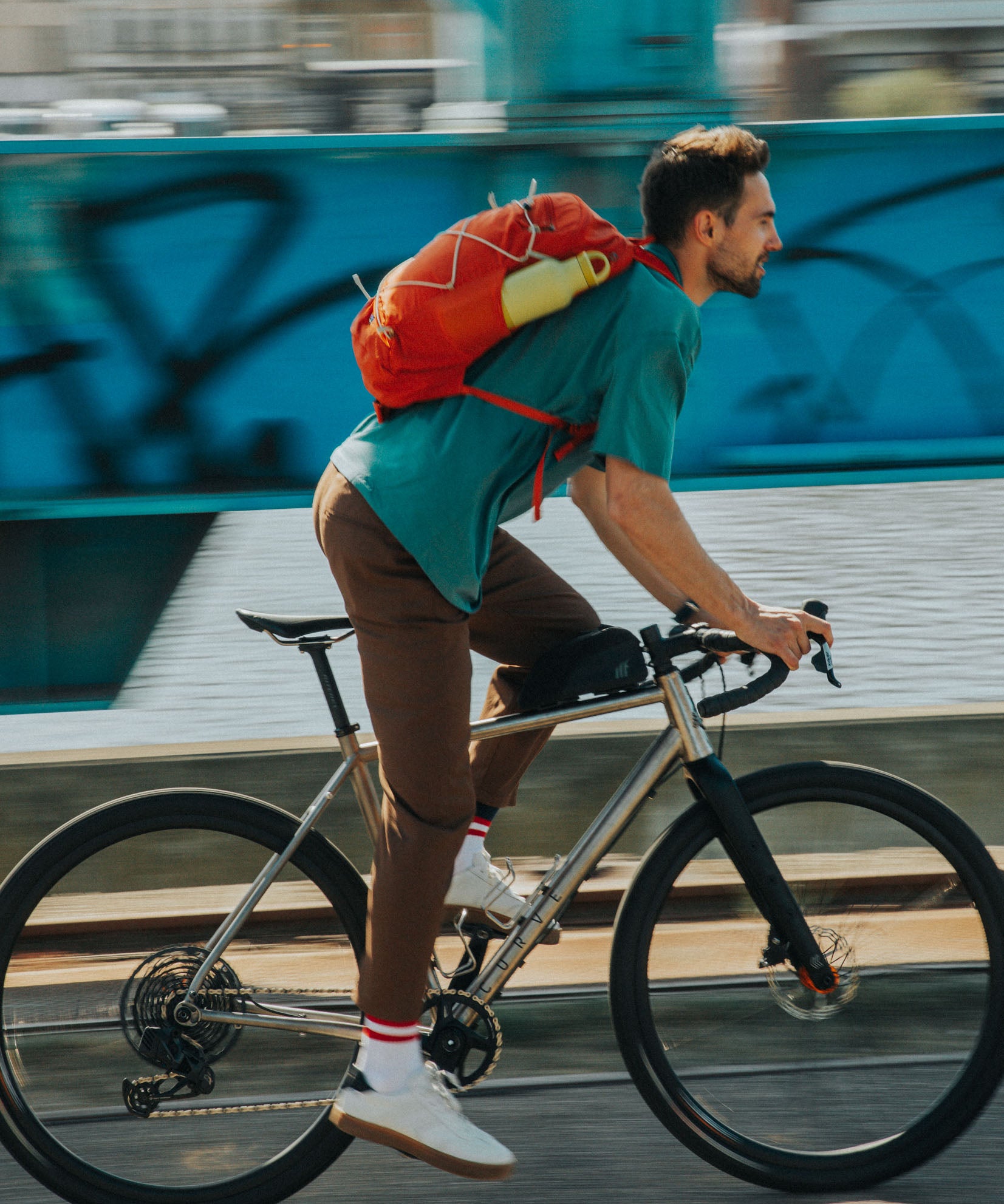 A man on a bike cycling with the acacia Klean Kanteen 20oz classic rise bottle in a bottle holder on a bag. A Reusable Stainless Steel Water Bottle with loop cap 