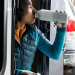 A woman sitting outside and drinking from the barely blue 20oz Klean Kanteen water bottle. 