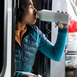 A woman sitting outside and drinking from the barely blue 20oz Klean Kanteen water bottle. 