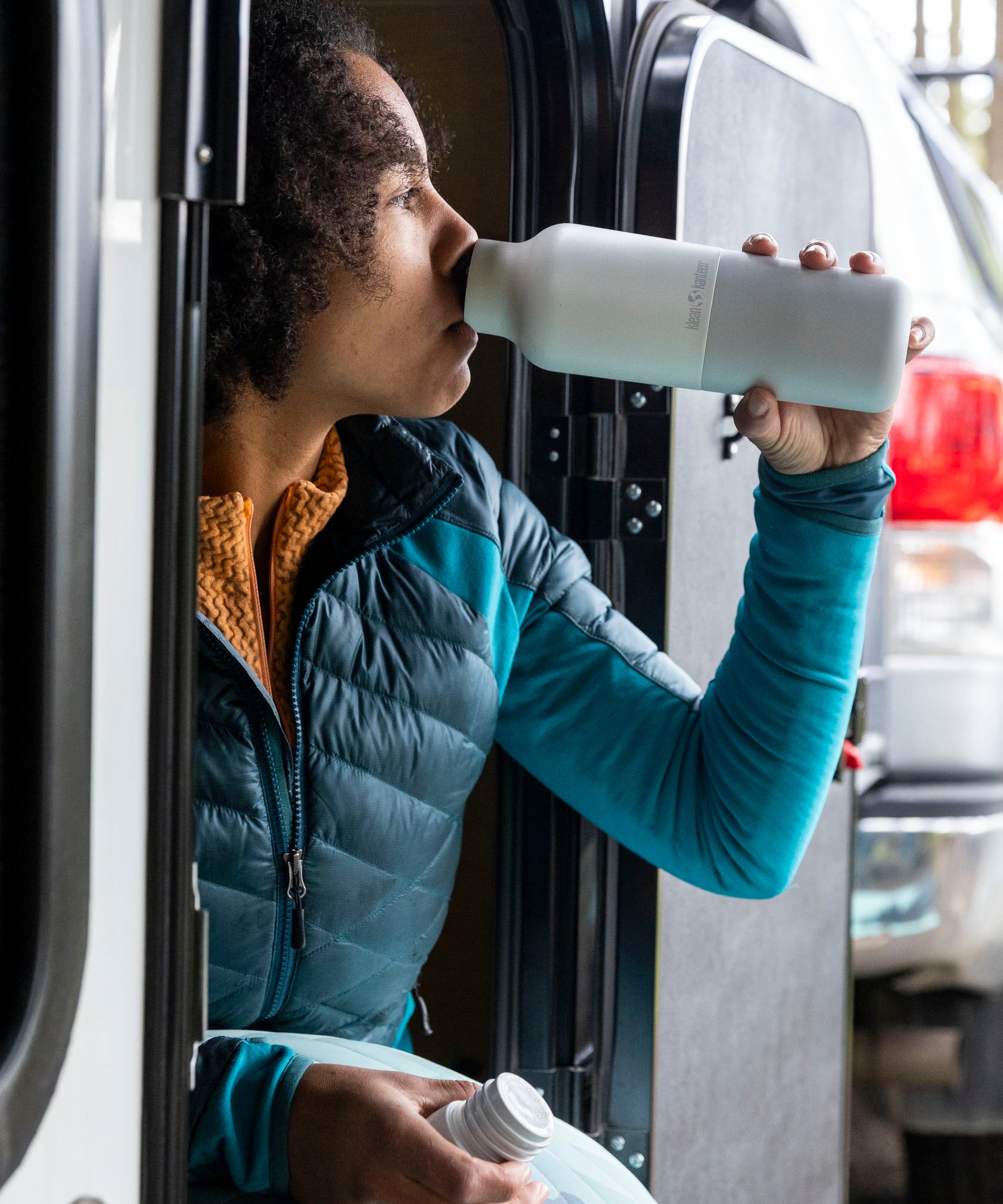 A woman sitting outside and drinking from the barely blue 20oz Klean Kanteen water bottle. 