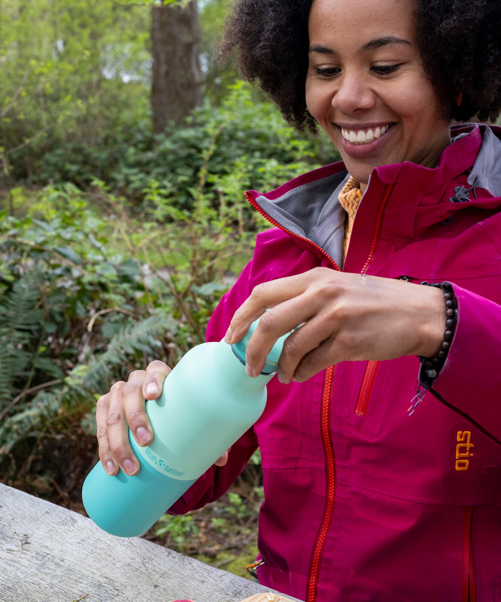 A woman sitting by the woodsand closing the loop cap on the Klean Kanteen 20oz cabbage rise bottle