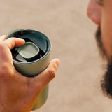 Man holding a Klean Kanteen 26oz sea spray green tumbler with a large 90mm rise slide lid on top