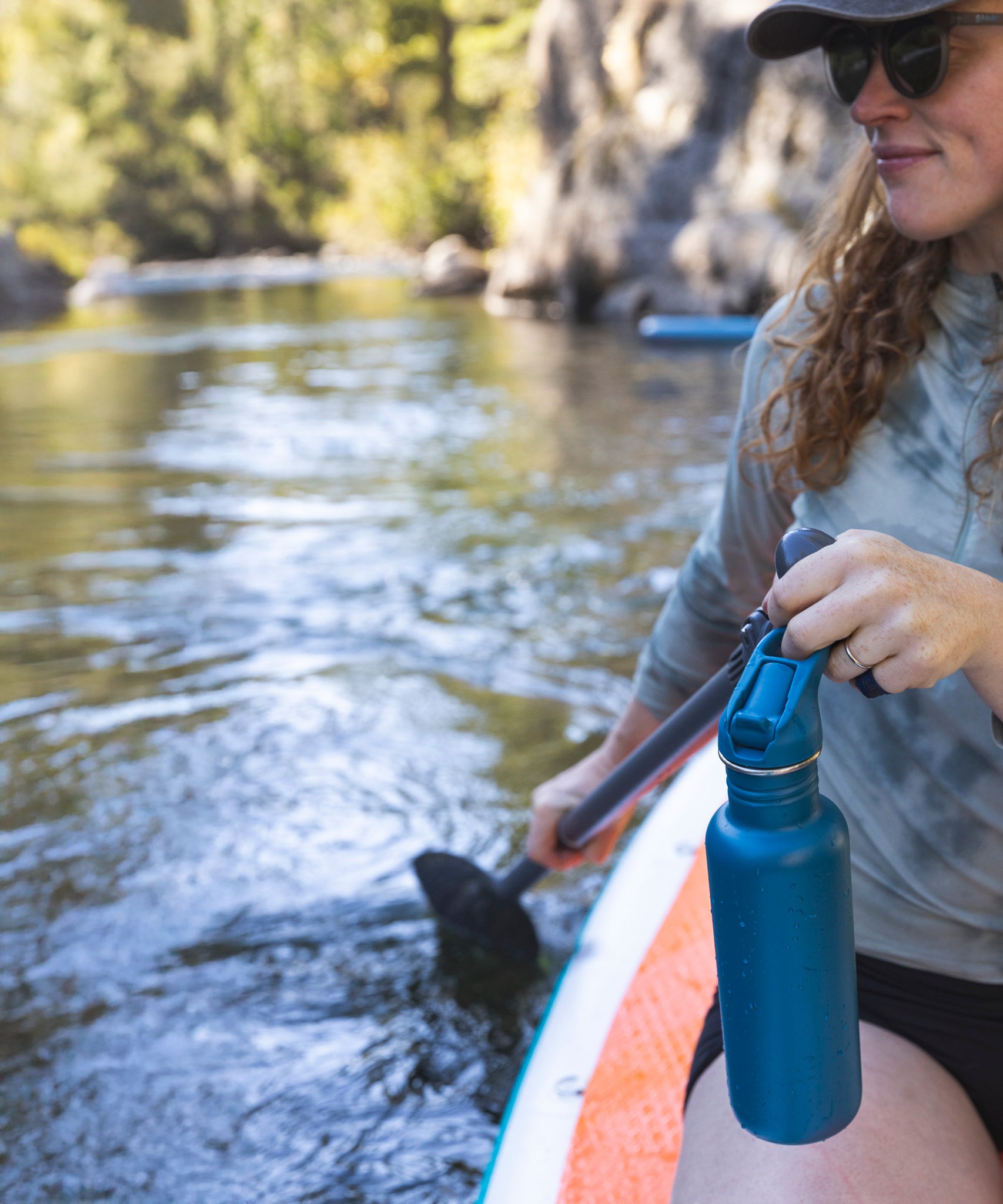 A person on the water holding a Corsair blue coloured Klean Kanteen 27oz Classic Narrow Flip Seal Sports Cap Reusable Stainless Steel Water Bottle in their hand.