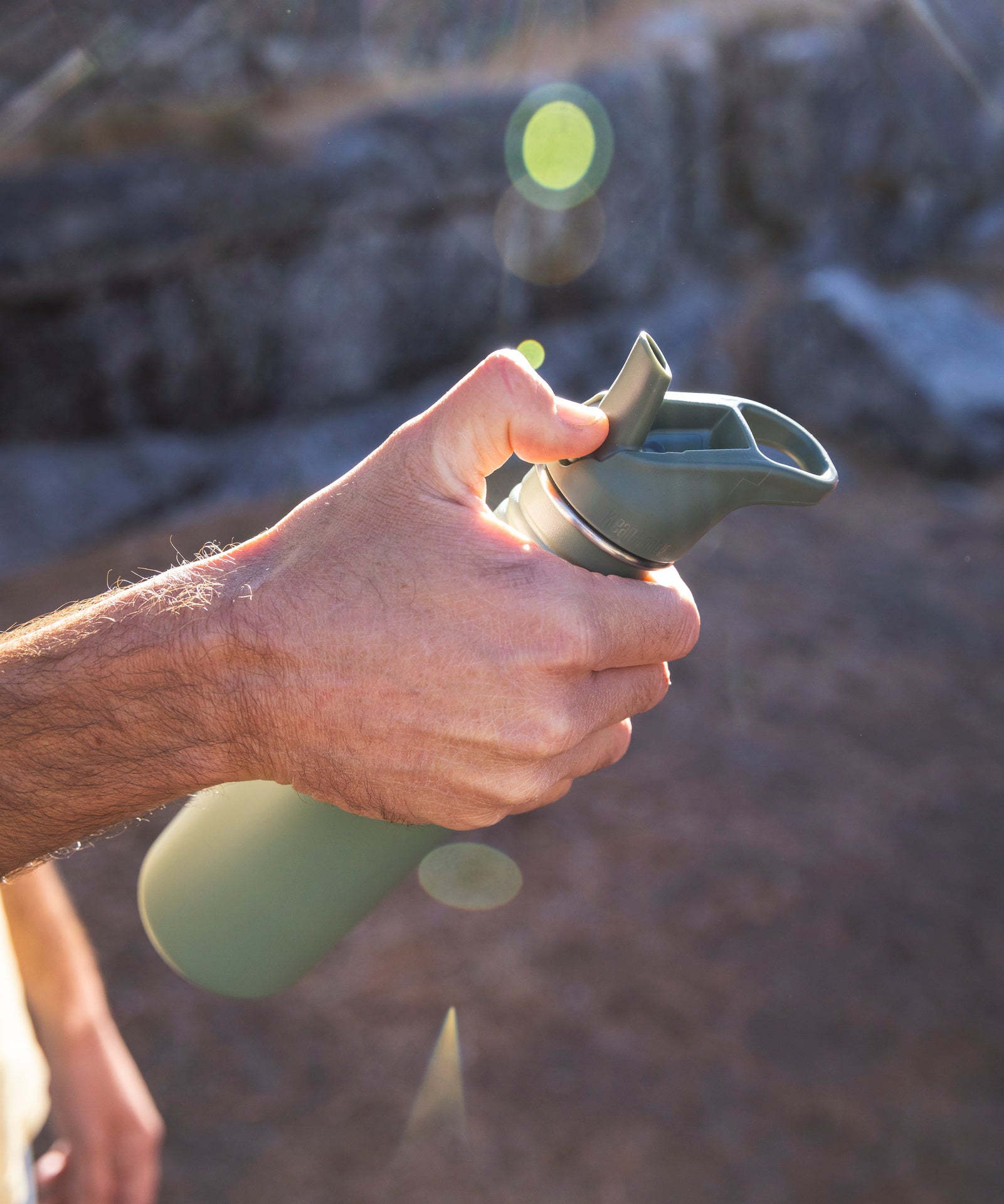 A close up of an adult holding a Sea Spray green coloured Klean Kanteen 27oz Classic Narrow Flip Seal Sports Cap Reusable Stainless Steel Water Bottle. They are opening the spout on the flip lid. 