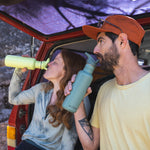 Two people sitting on teh boot of a red car drinking from Klean Kanteen 27oz Classic Narrow Flip Seal Sports Cap Reusable Stainless Steel Water Bottles. One is Shadow Lime and the other is Sea Spray. 