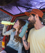 Two people sitting on teh boot of a red car drinking from Klean Kanteen 27oz Classic Narrow Flip Seal Sports Cap Reusable Stainless Steel Water Bottles. One is Shadow Lime and the other is Sea Spray. 