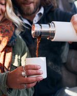 Close up of a man and woman pouring some liquid into the cup of a Klean kanteen 500ml tkpro insulated flask