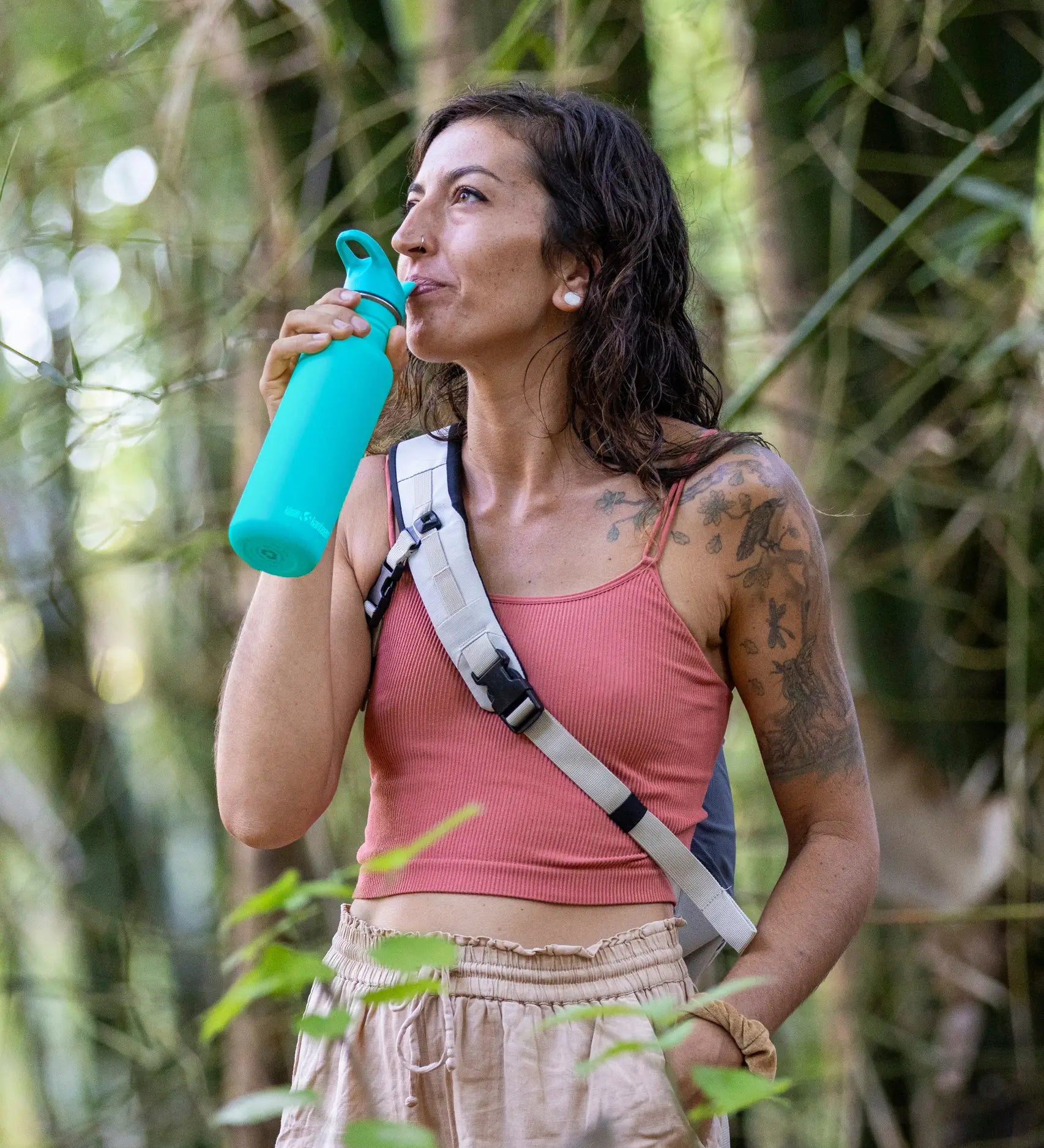 Woman standing in the forest and drinking out of the Klean Kanteen baltic blue 27oz stainless steel water bottle