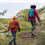 2 adult walkers outside walking on a cliff and holding the Brittany blue and iceberg stainless reusable water Klean Kanteen 20oz bottles 