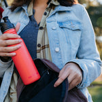 Close up of a woman putting a Klean Kanteen single wall steel bottle with a sports lid into a rucksack