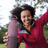 Adult holding a dusty orchid Klean Kanteen 20oz insulated bottle with matching lid outdoors