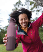Adult holding a dusty orchid Klean Kanteen 20oz insulated bottle with matching lid outdoors