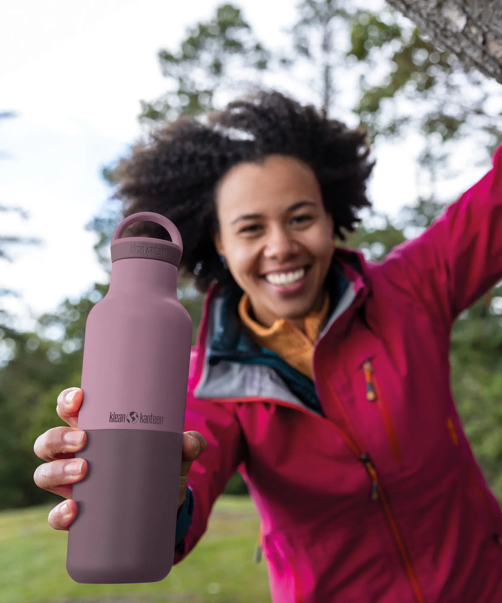 Adult holding a dusty orchid Klean Kanteen 20oz insulated bottle with matching lid outdoors