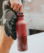 Adult holding a garnet red Klean Kanteen 20oz insulated bottle with matching lid and climbing shoes