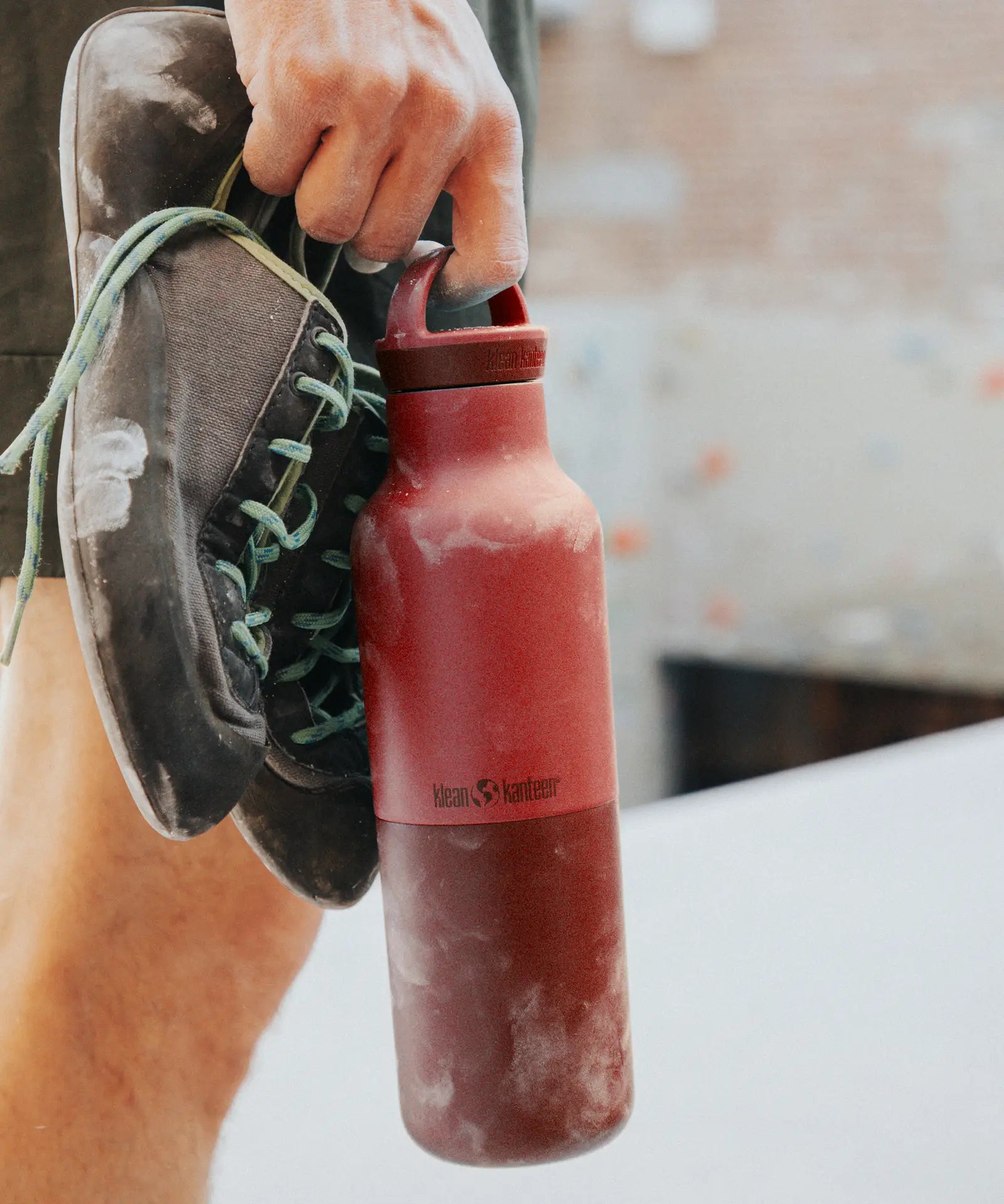 Adult holding a garnet red Klean Kanteen 20oz insulated bottle with matching lid and climbing shoes